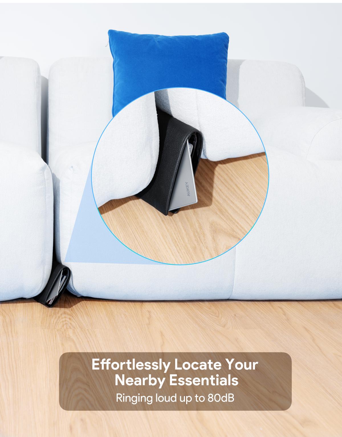 AUKEY TM-21 Track Mate 3 smart Bluetooth tracker attached to a black wallet behind a white couch on wooden floor